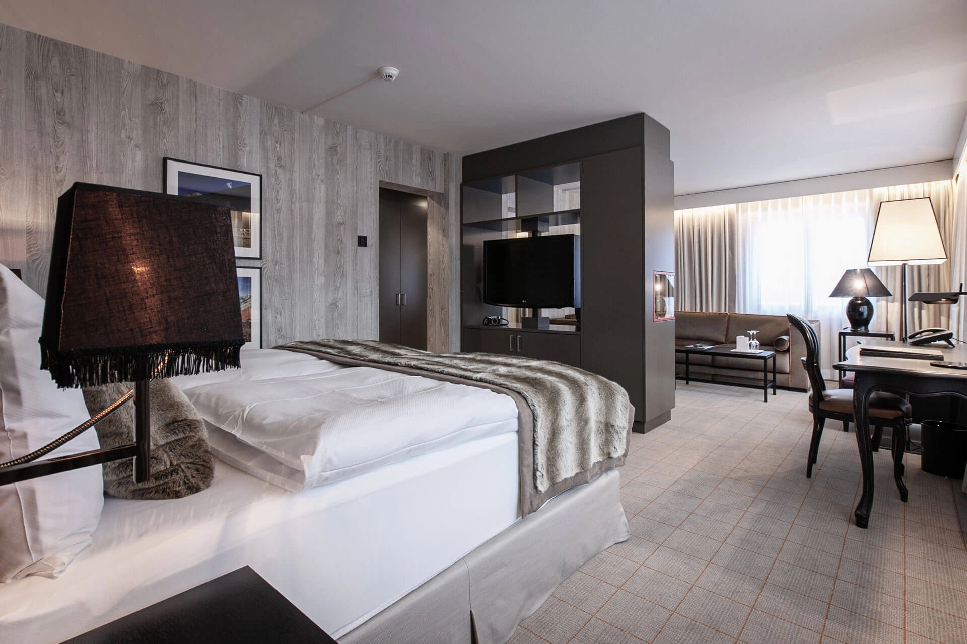 Helles, modernes Hotelzimmer mit großem Doppelbett, Schreibtisch, Fernseher und separater Sitzecke am Fenster.