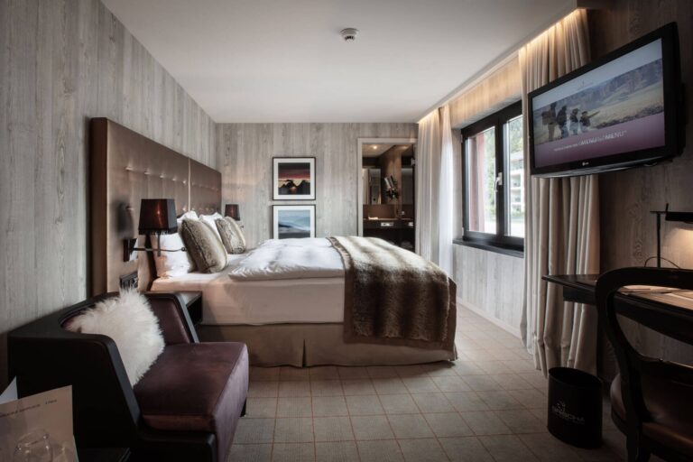 Double room at Hotel Grischa with upholstered bed, fur throw, leather armchair, and flat screen