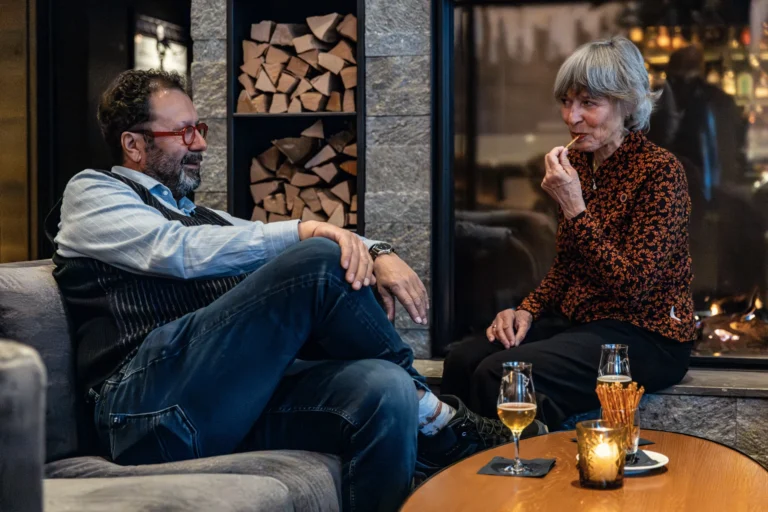 Zwei Gäste im Gespräch mit Weisswein vor dem Kamin in der Lounge