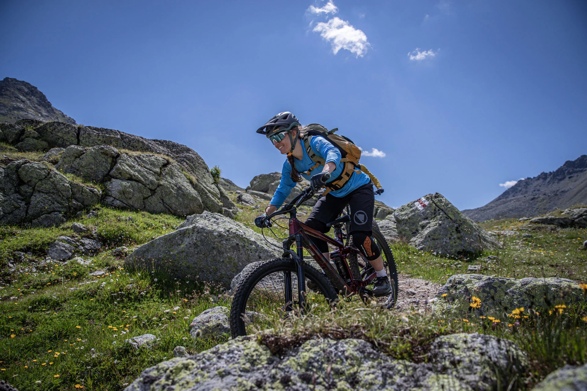 Mountainbikerin fährt über einen Trail durch eine felsige Bergwiese