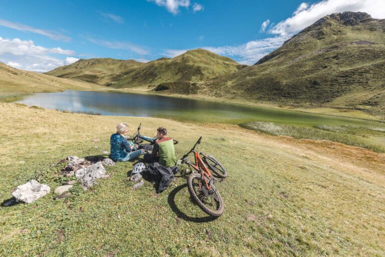 Zwei Mountainbiker rasten mit ihren E-Bikes an einem Bergsee bei Davos