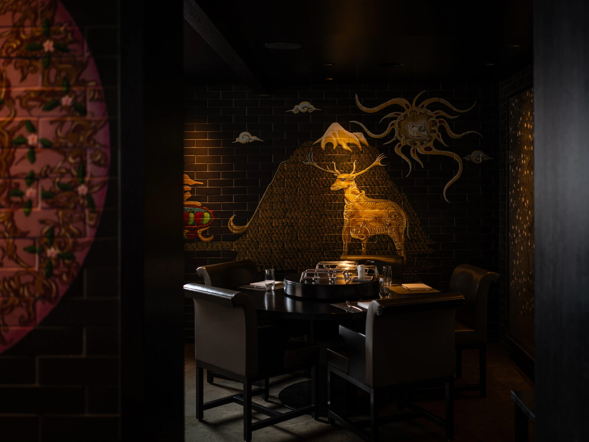 Exklusiver Sitzbereich im Golden Dragon mit rundem Tisch, dunkler Einrichtung und kunstvoll gestalteter asiatischer Wandmalerei.