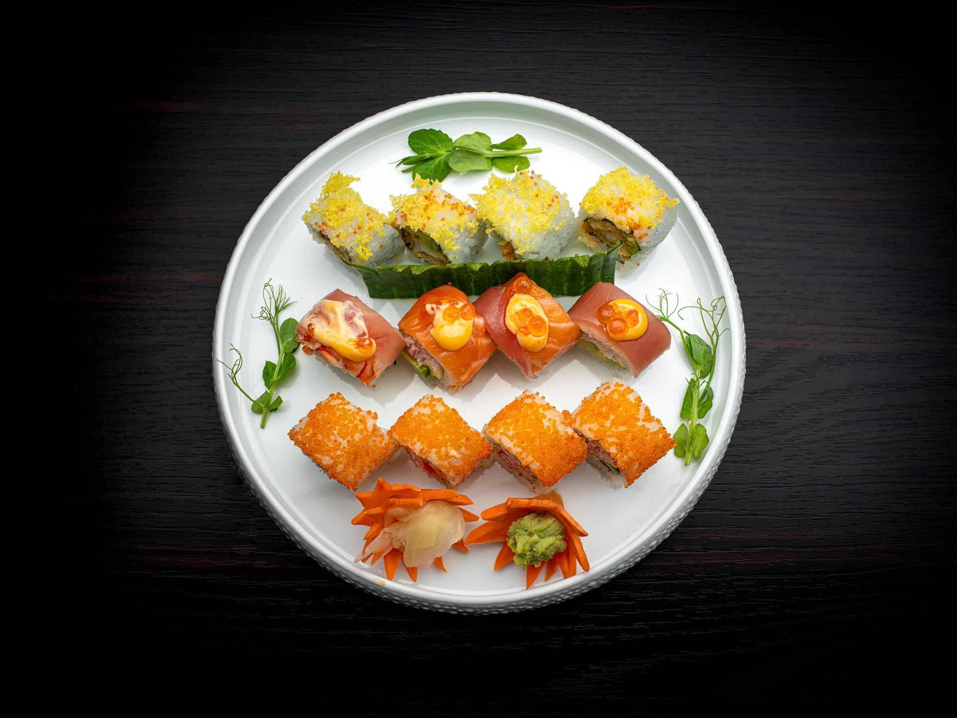 Verschiedene farbige Sushis auf einem weissen Teller mit Kräutern als Dekoration.