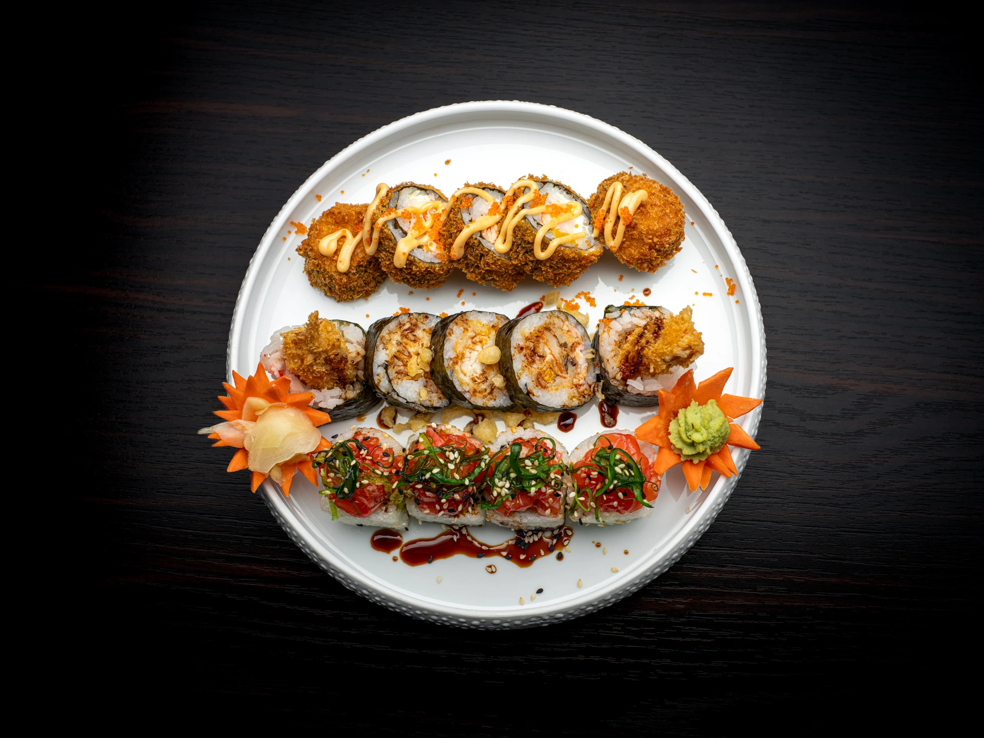 Auswahl an frisch zubereiteten Sushi-Rollen mit knusprigen, flambierten und würzig marinierten Variationen, kunstvoll angerichtet auf einem Teller.