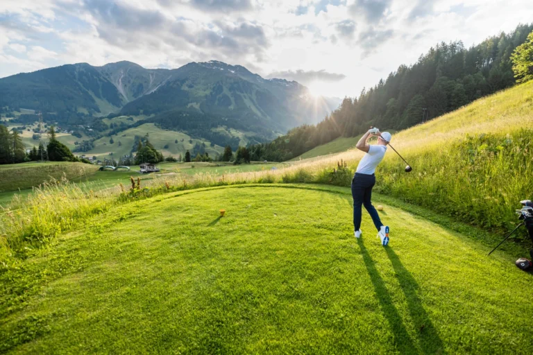 Golfer teeing off on Klosters golf course in the evening light