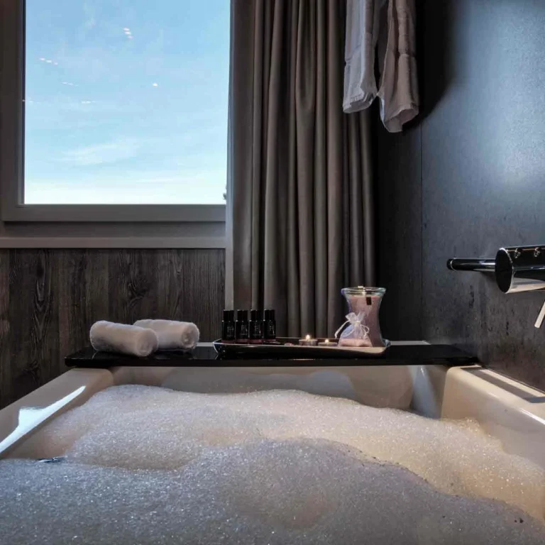 Bathtub with bubble bath, toiletries, and window view