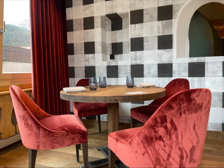 Runder Holztisch mit roten Samtsesseln vor der Karo-Wand im Restaurant Bräma