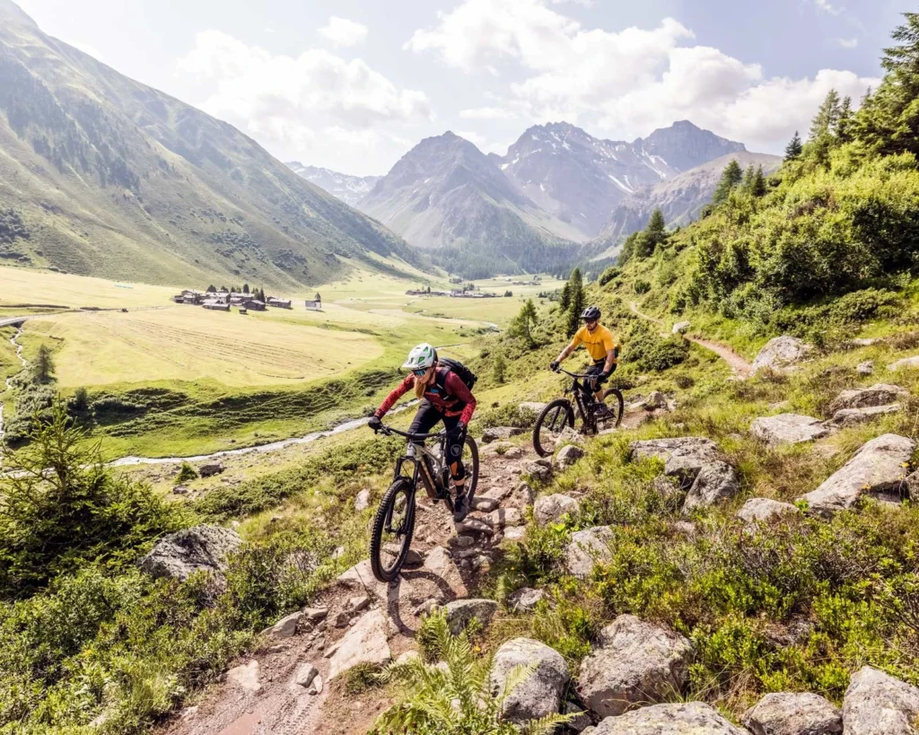 Zwei Mountainbiker fahren einen Trail hinunter ins Tal bei Davos