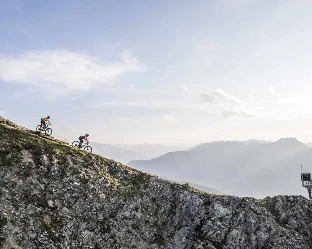 Zwei Mountainbiker auf einem Gratweg hoch über dem Tal im Abendlicht