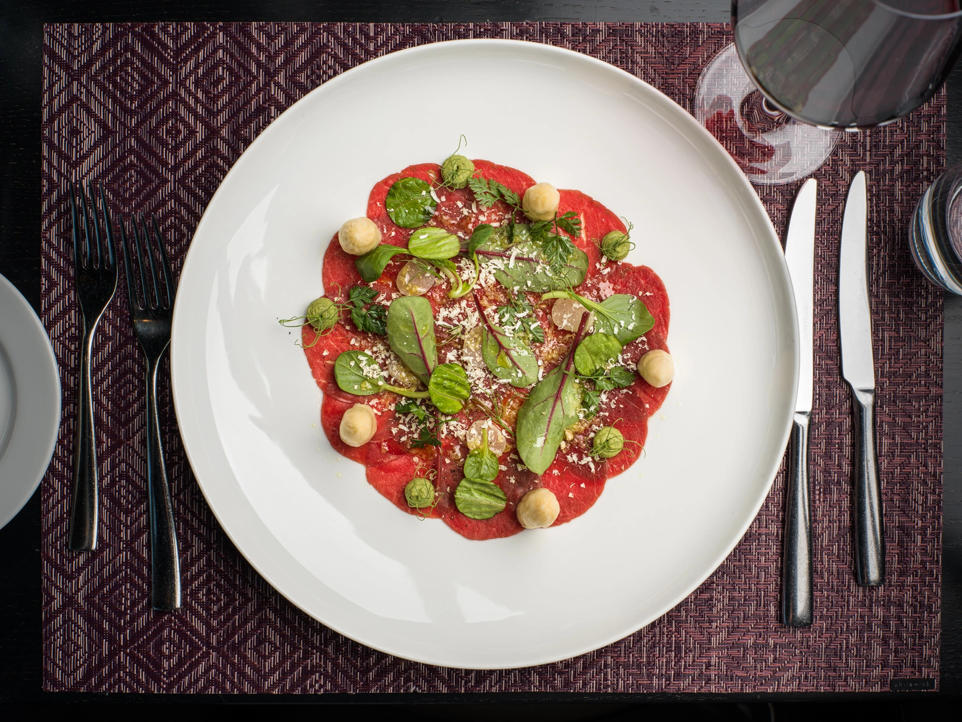 Feines Rindercarpaccio mit Kräutern, Parmesan und cremigen Tupfen als Vorspeise im Restaurant Pulsa.