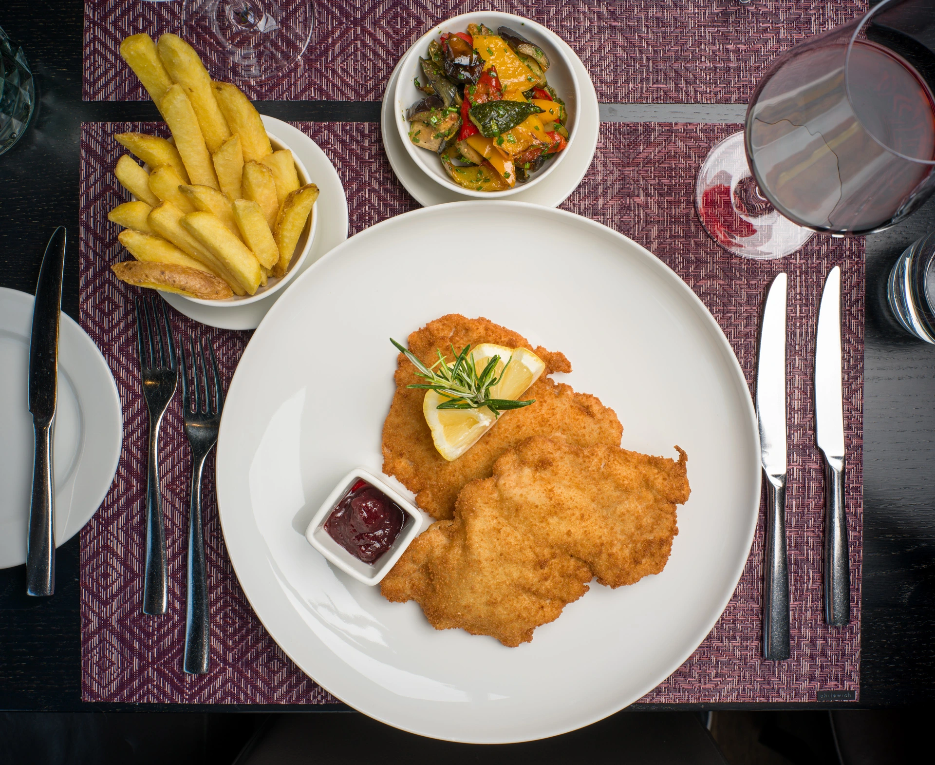 Knuspriges Kalbsschnitzel mit Pommes frites, Preiselbeeren und mediterranem Gemüse im Restaurant Pulsa.