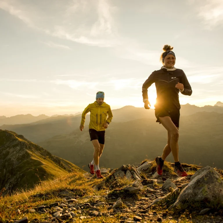 Two trail runners running across a mountain ridge at sunrise