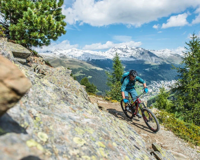 Mountainbiker fährt einen Trail oberhalb von Davos mit Blick auf die Stadt