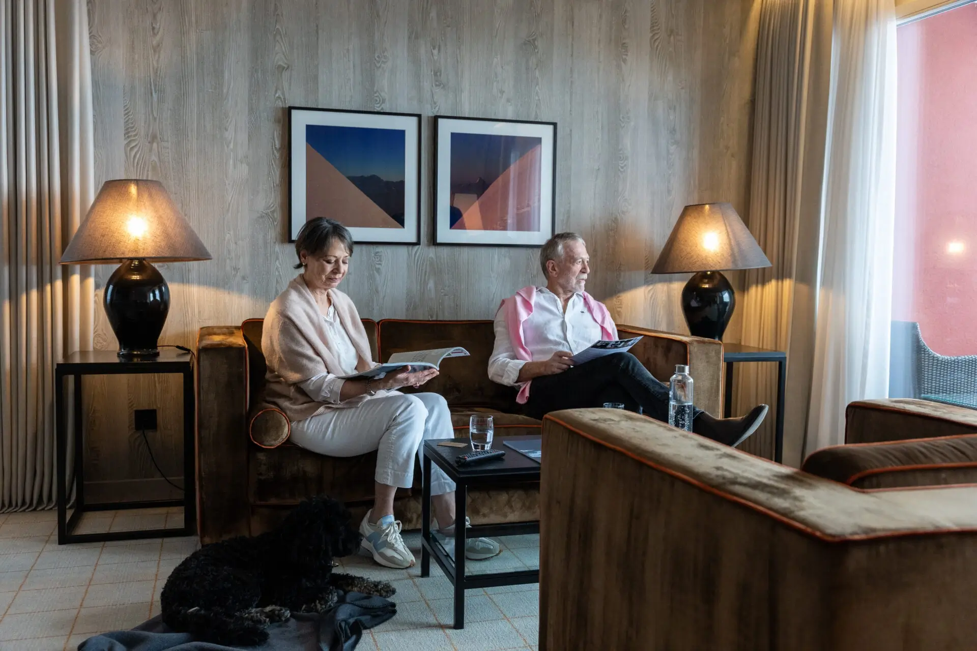 Zwei Gäste lesen mit ihrem Hund in der Lounge des Hotel Grischa