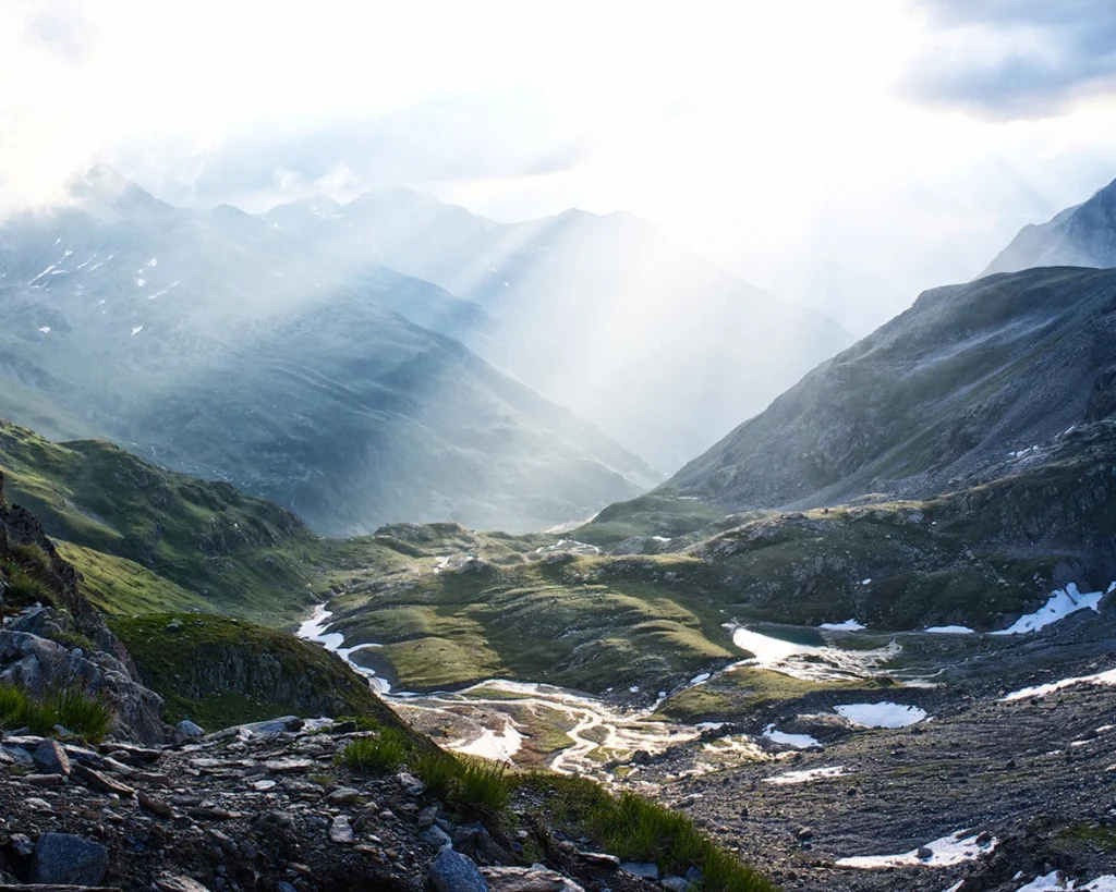Sonnenstrahlen durchbrechen die Wolken über einem Bergtal bei Davos