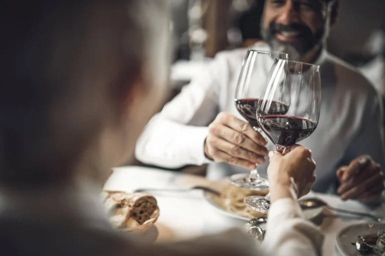 Guests clink red wine glasses at the table