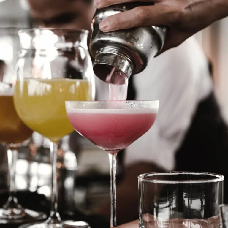 Bartender pours a pink cocktail from the shaker into a coupe glass