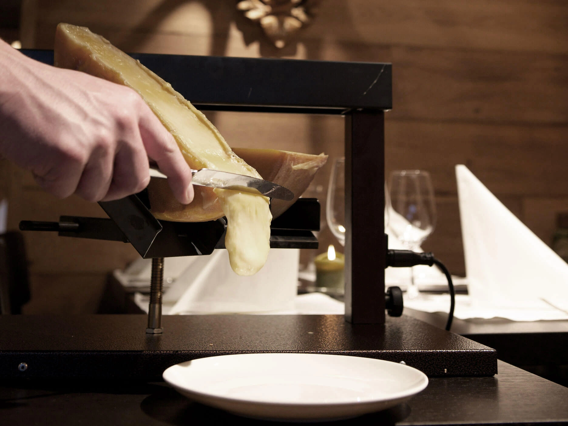 Ein Messer streicht den Raclette-Käse vom grossen Raclette-Ofen ab.