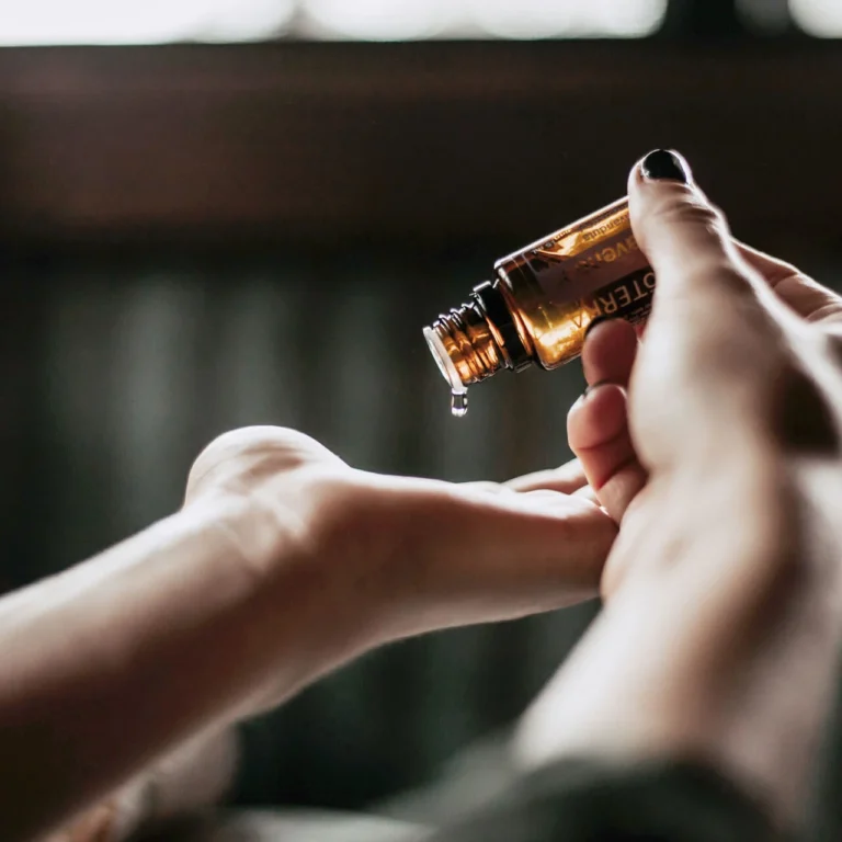 Massage oil is dripped from a small bottle onto the hand