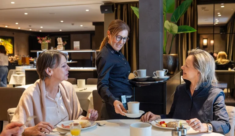 Service staff member serving coffee to two guests in the restaurant