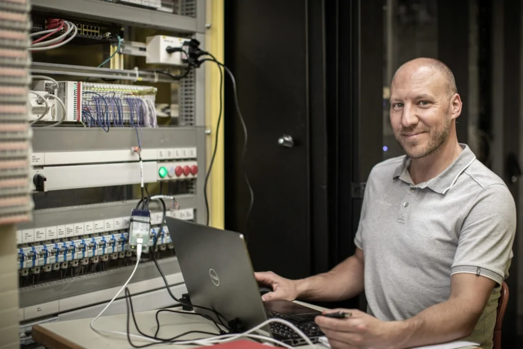 Porträt von Sandro am Laptop vor einem Technikschrank