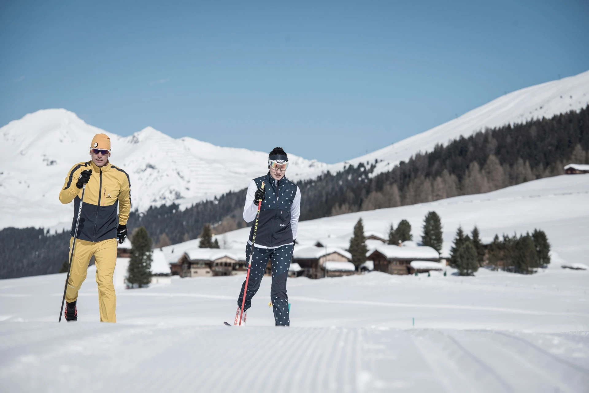Zwei Langläufer auf der Loipe vor einem verschneiten Dorf