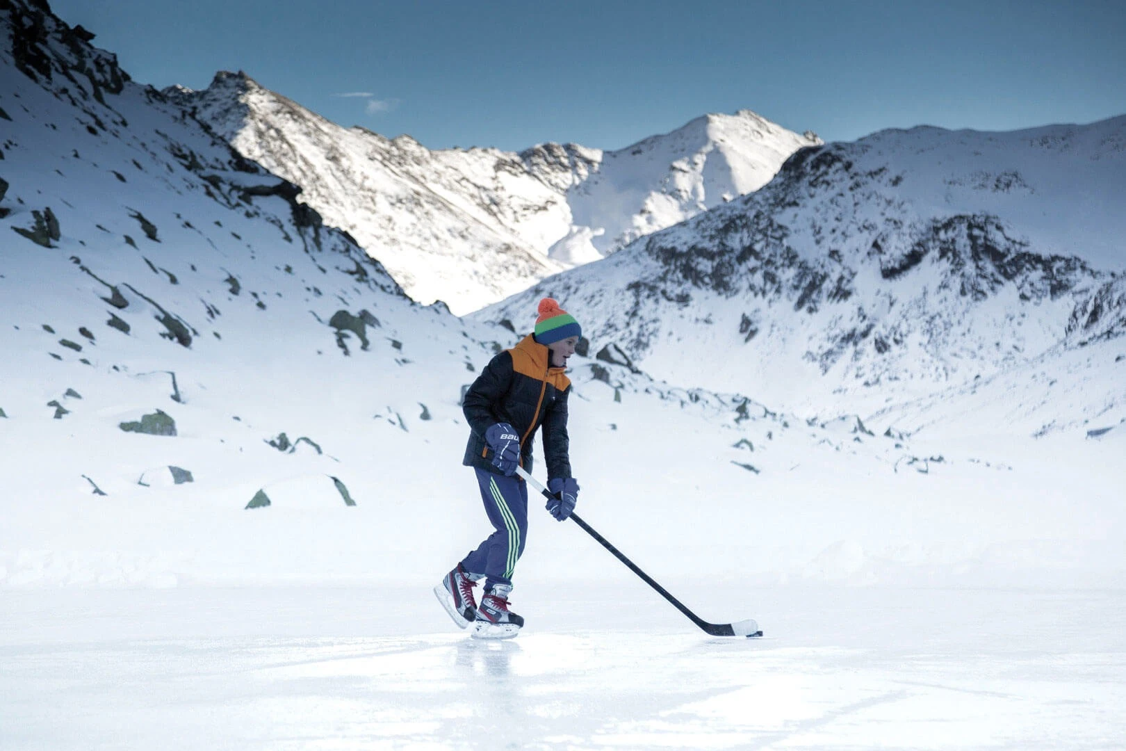Eishockeyspieler auf einem zugefrorenen Bergsee vor verschneiten Gipfeln