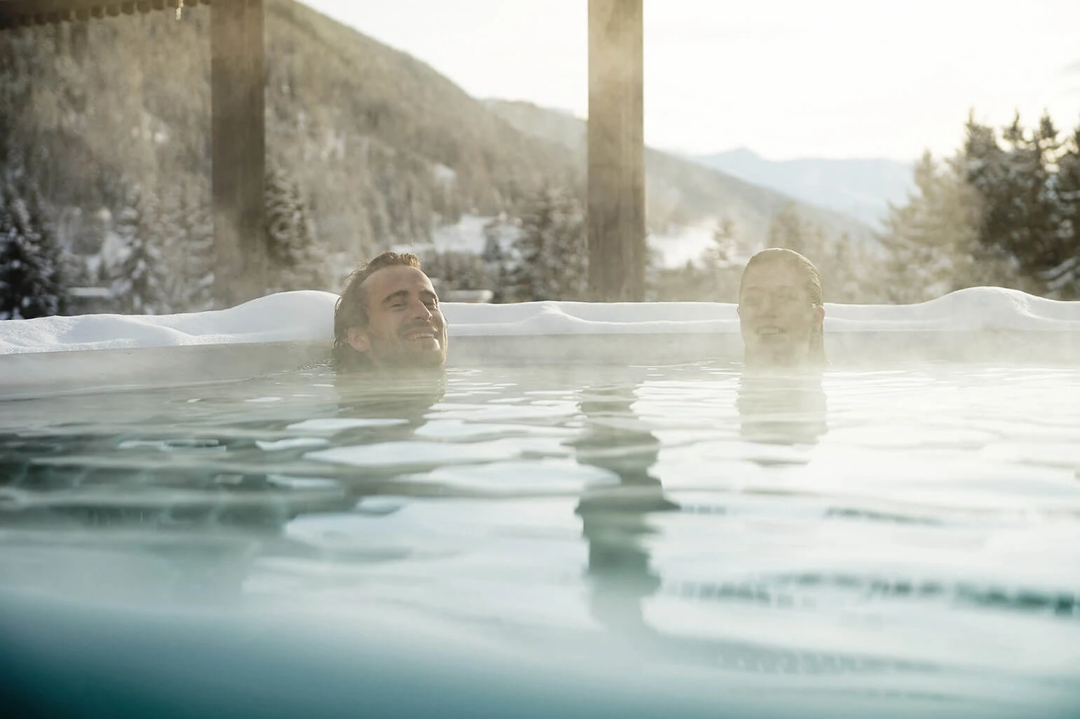 Zwei Personen im warmen Aussenpool mit Blick auf die verschneite Landschaft