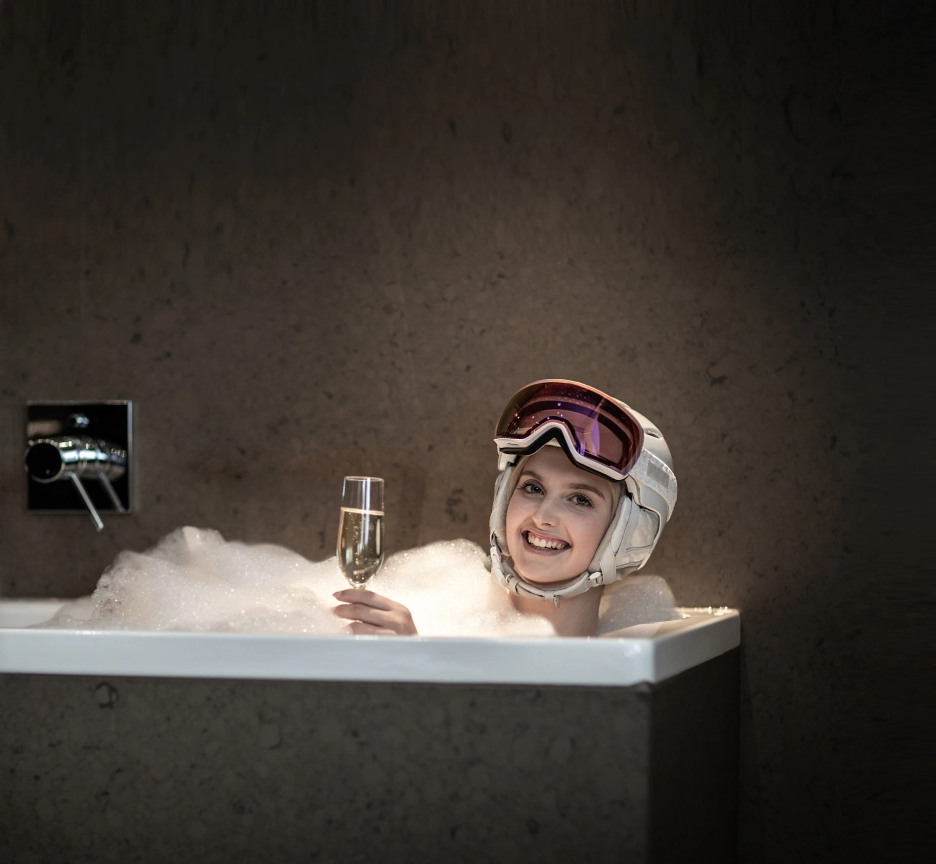 Person mit Skibrille und einem Glas Schaumwein im Schaumbad