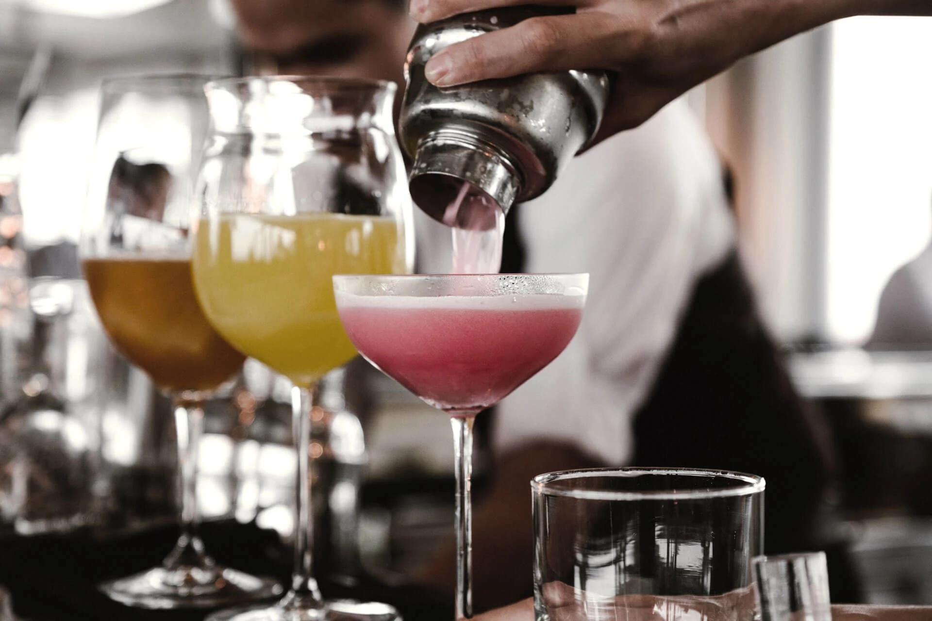 Barkeeper giesst einen rosa Cocktail aus dem Shaker in ein Coupe-Glas