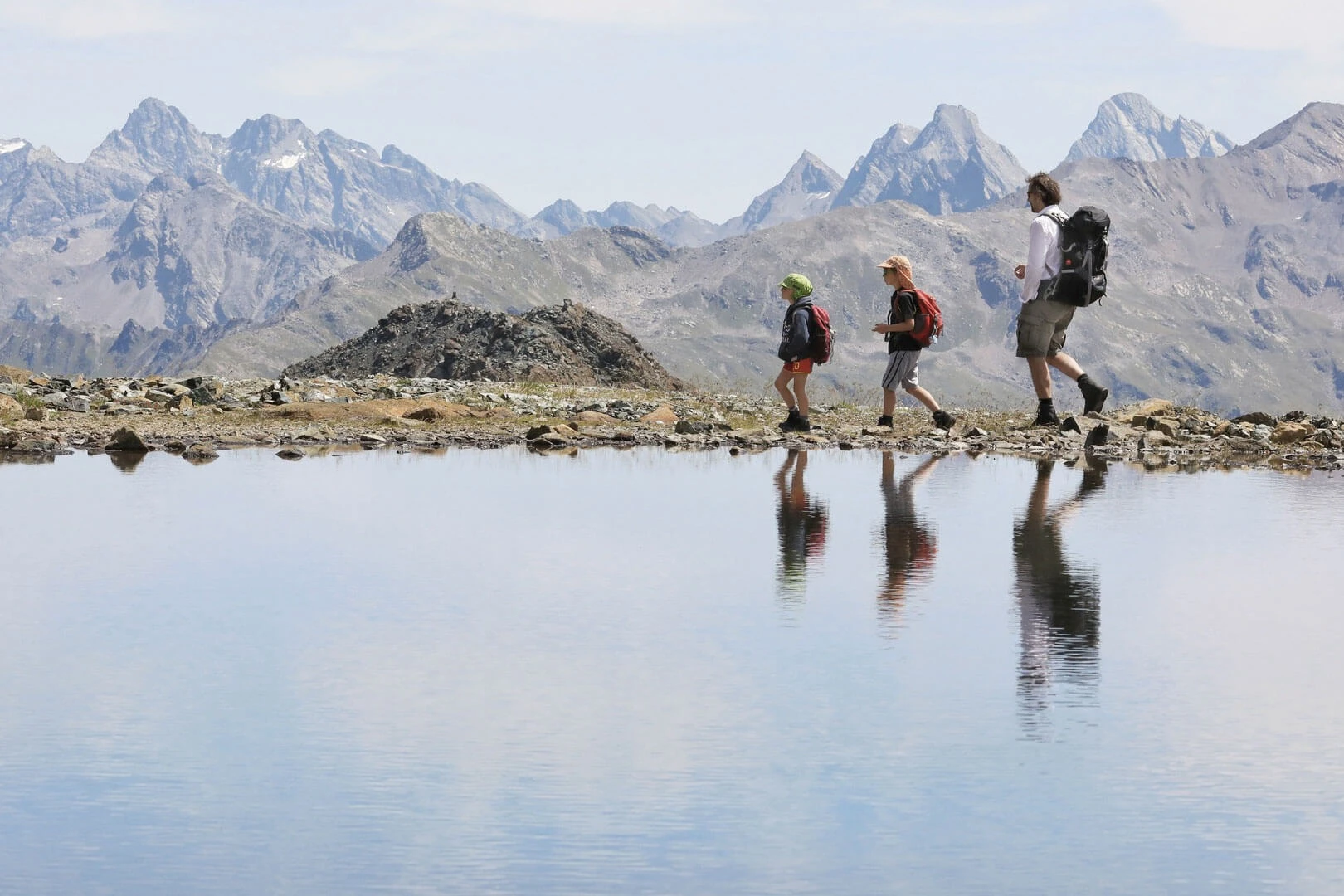 Drei Wandernde spiegeln sich im Wasser eines Bergsees