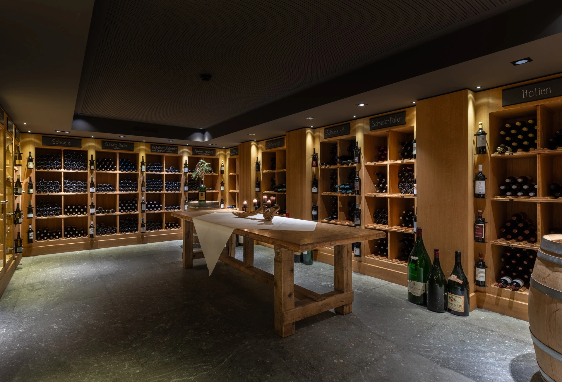 Weinkeller des Hotel Grischa mit Holztisch, Regalen und Grossflaschen
