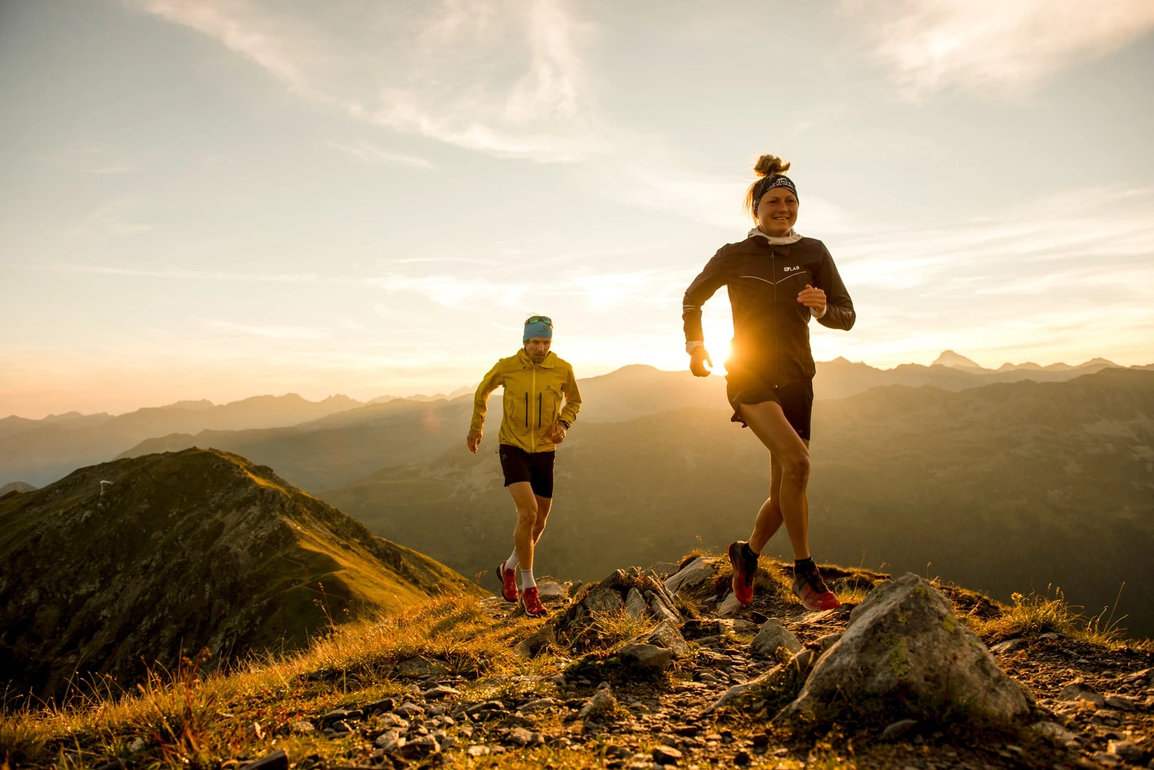 Zwei Trailrunner laufen bei Sonnenaufgang über einen Bergkamm