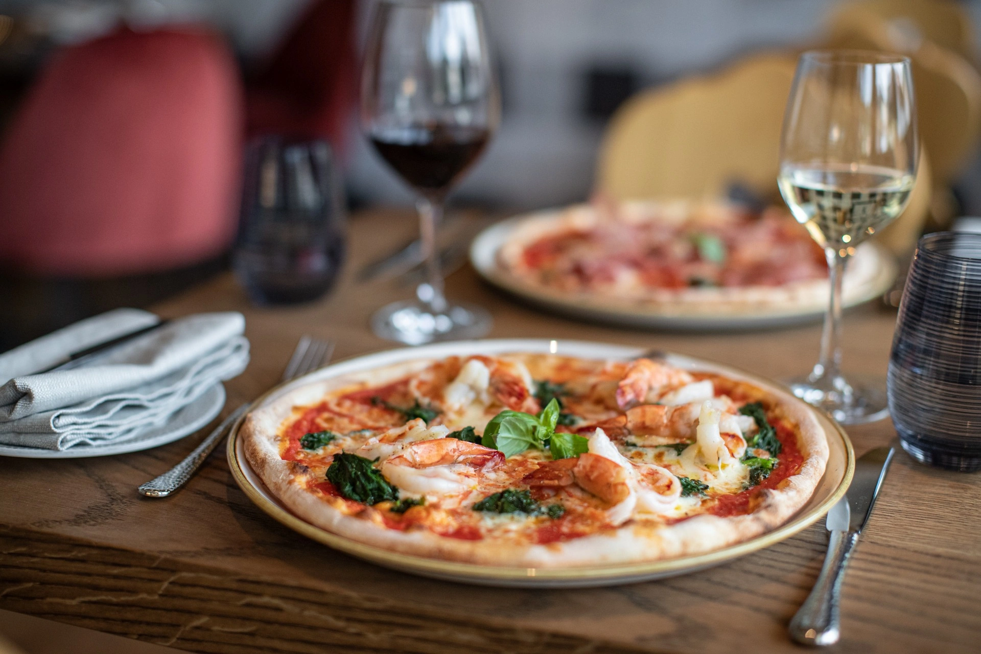 Pizza mit Hummer und Spinat auf einem bedeckten Tisch mit Wein.
