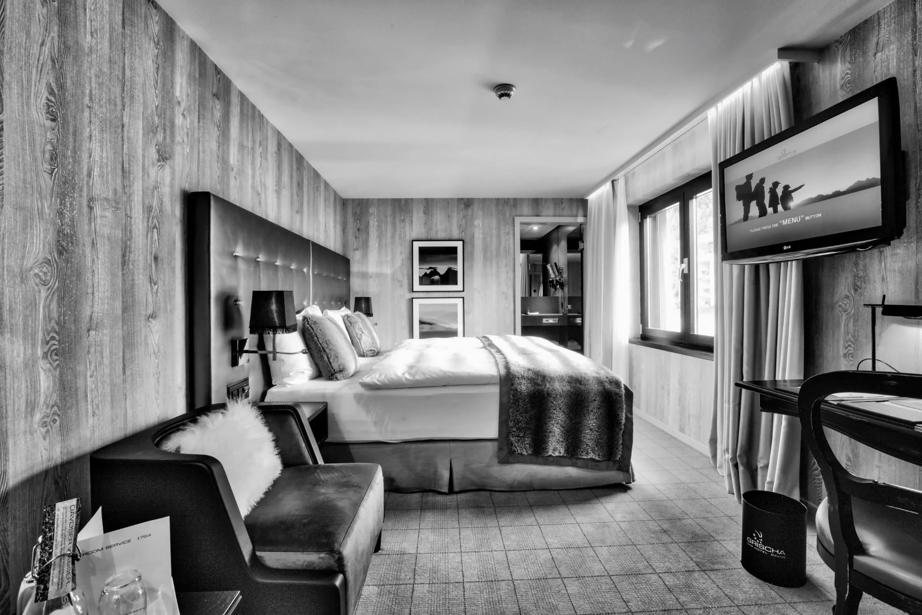 Hotelzimmer im Hotel Grischa mit Bett, Sessel und Flatscreen in Schwarz-Weiss