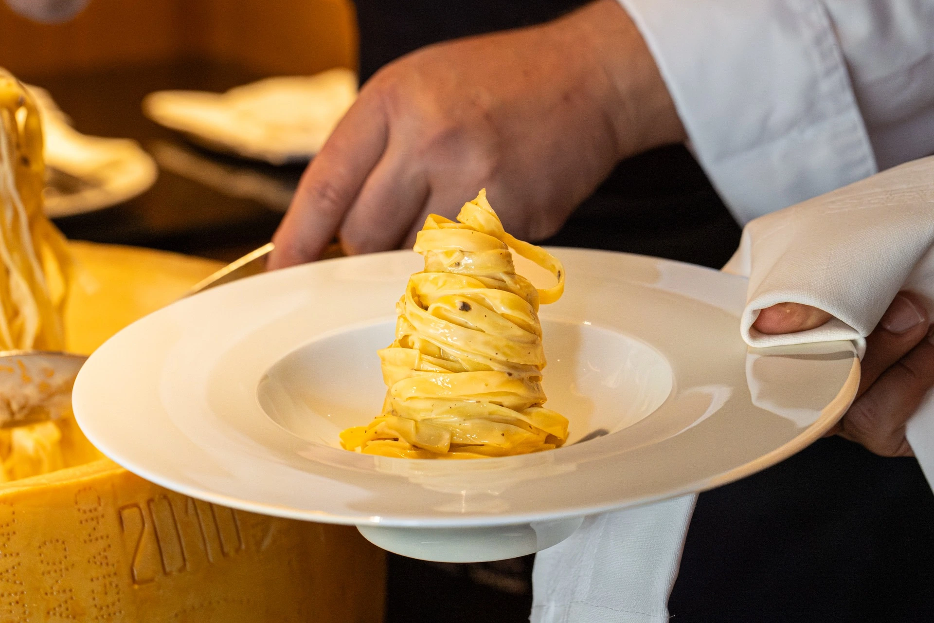 Koch serviert Tagliatelle, die im Parmesanlaib geschwenkt wurden