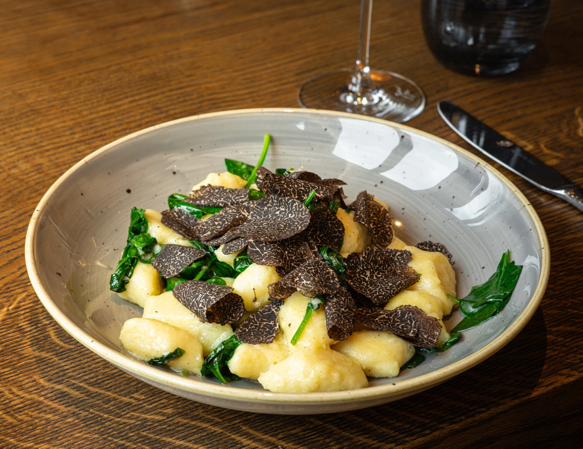 Hausgemachte Gnocchi mit frischem Blattspinat und großzügig gehobeltem schwarzem Trüffel in einer Keramikschale.
