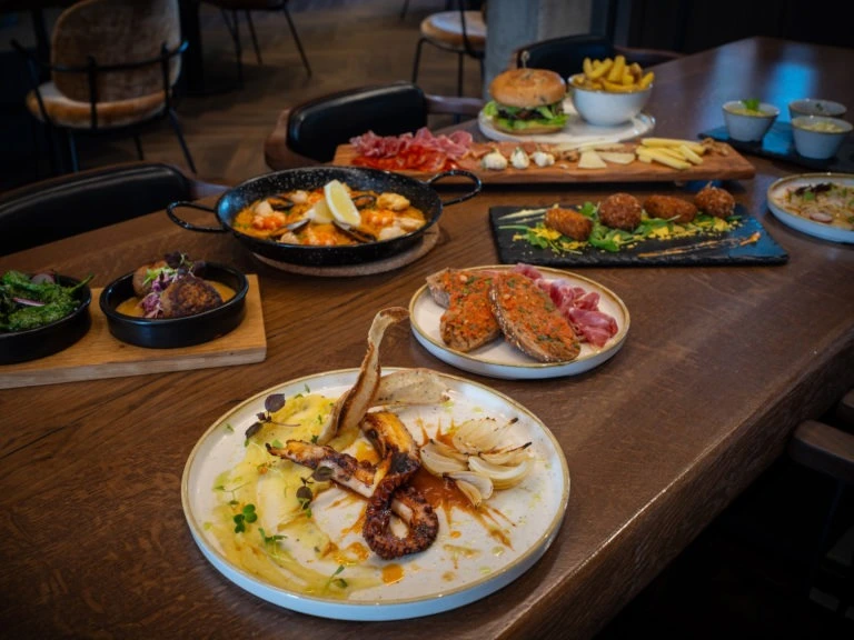 Holztisch mit verschiedenen Sharing-Gerichten, Burger, Tapas und Oktopus