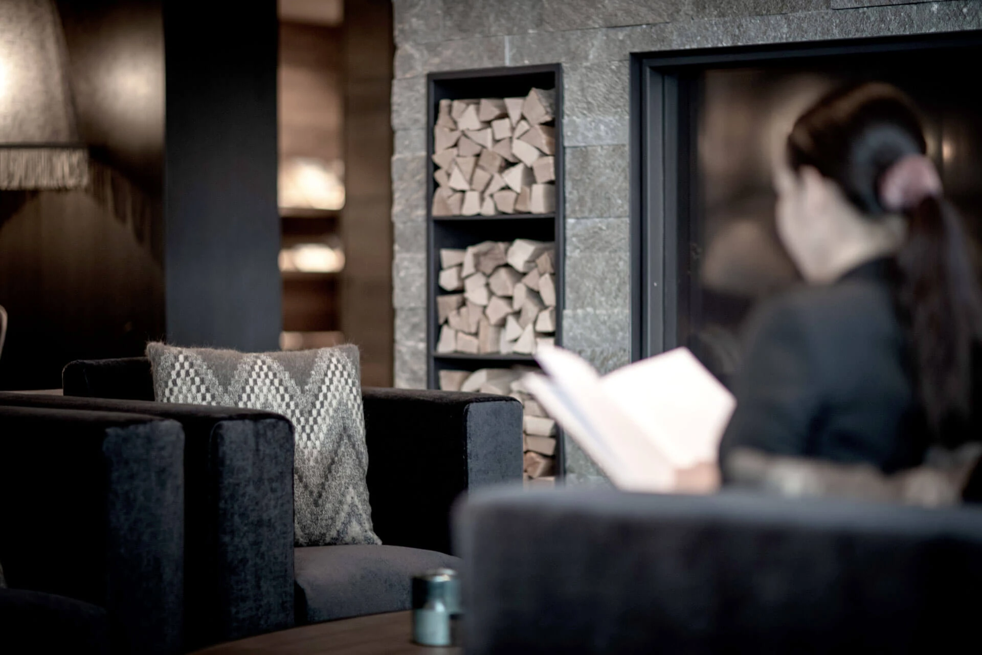 Frau liest ein Buch im Sessel vor dem Kamin in der Lounge