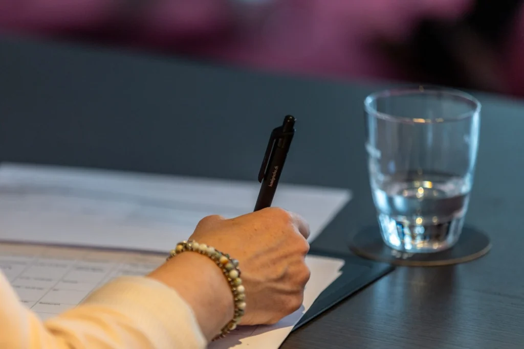 Hand notiert mit einem Kugelschreiber auf einem Formular, daneben ein Wasserglas