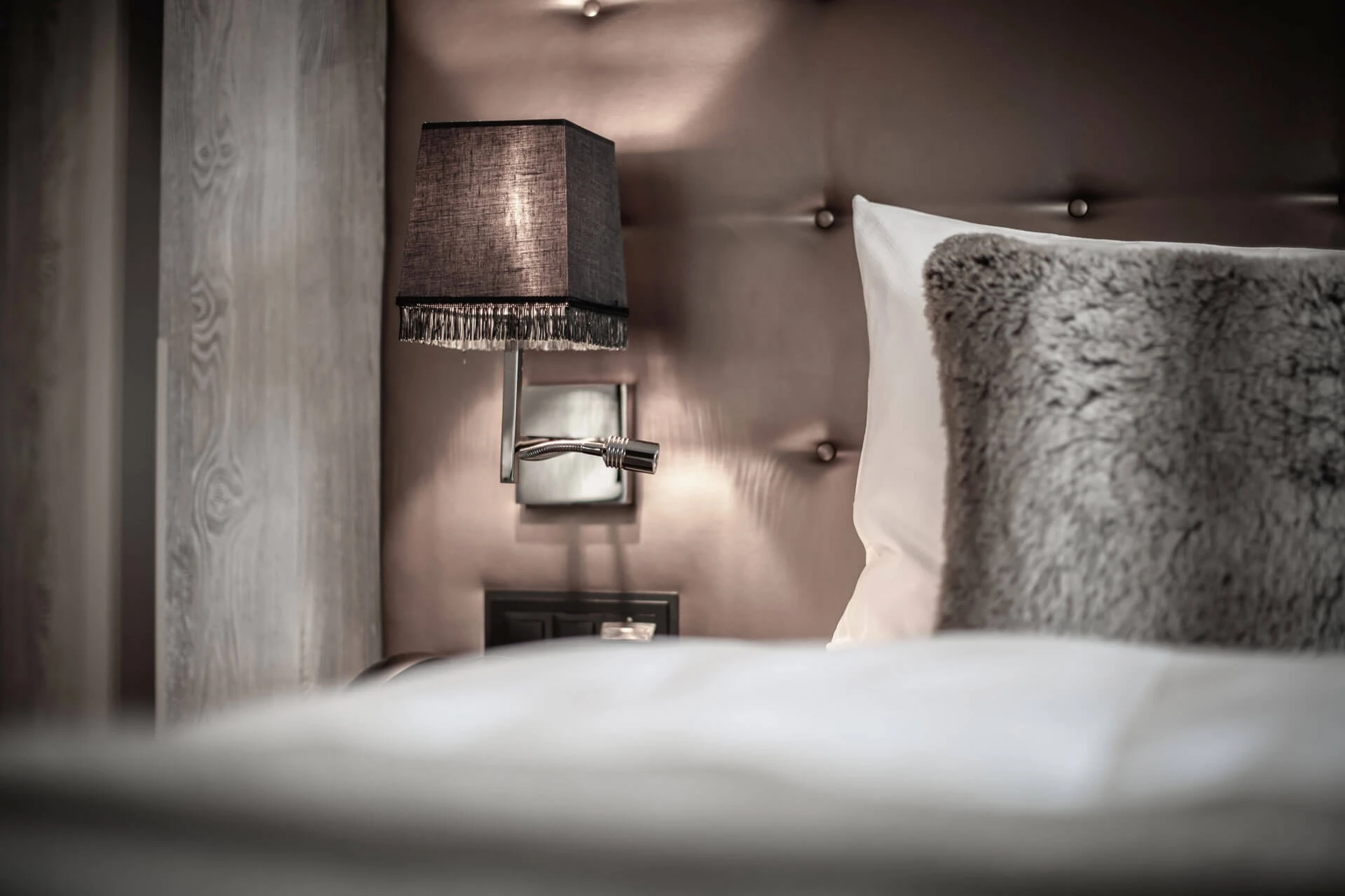 Bett mit Lederkopfteil, Wandleuchte und Fellkissen im Hotel Grischa